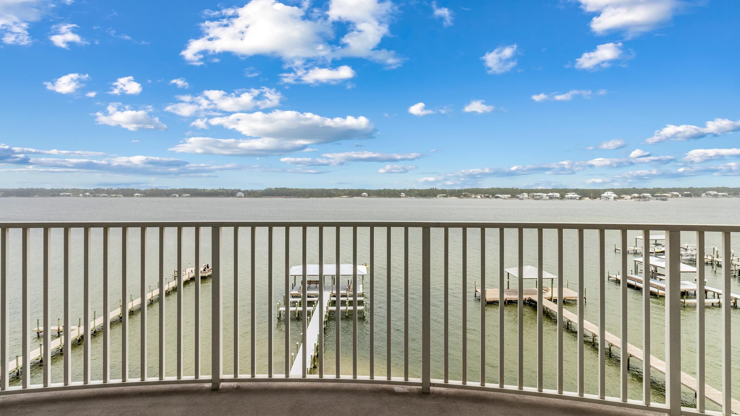 A waterfront view from a balcony with a railing, a dock, and a marina in the background.