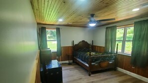 Une chambre avec un plafond en bois, un lit, une table de chevet et une fenêtre avec des rideaux.