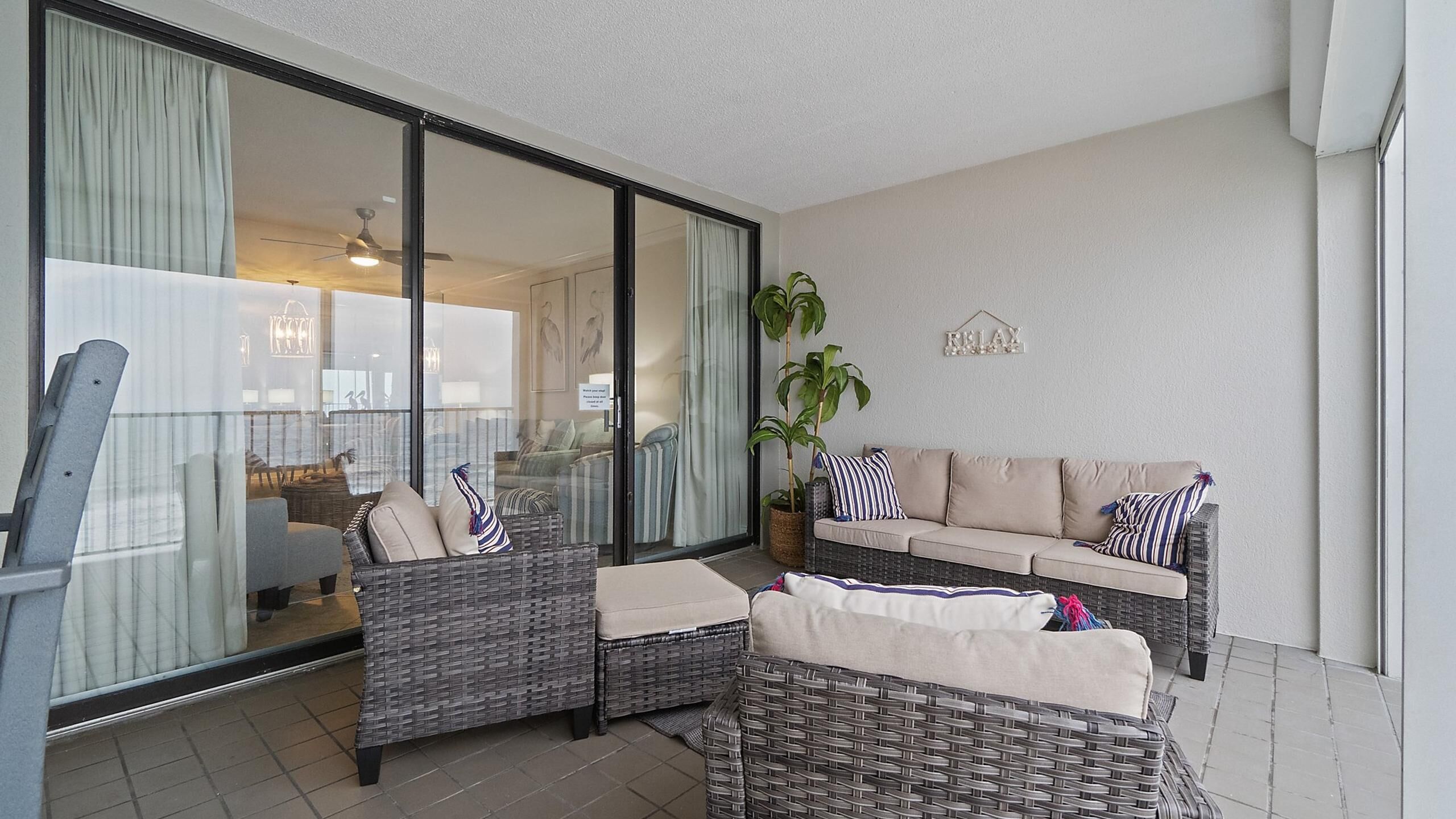 A balcony with wicker furniture, a potted plant, and a 'RELAX' sign on the wall.