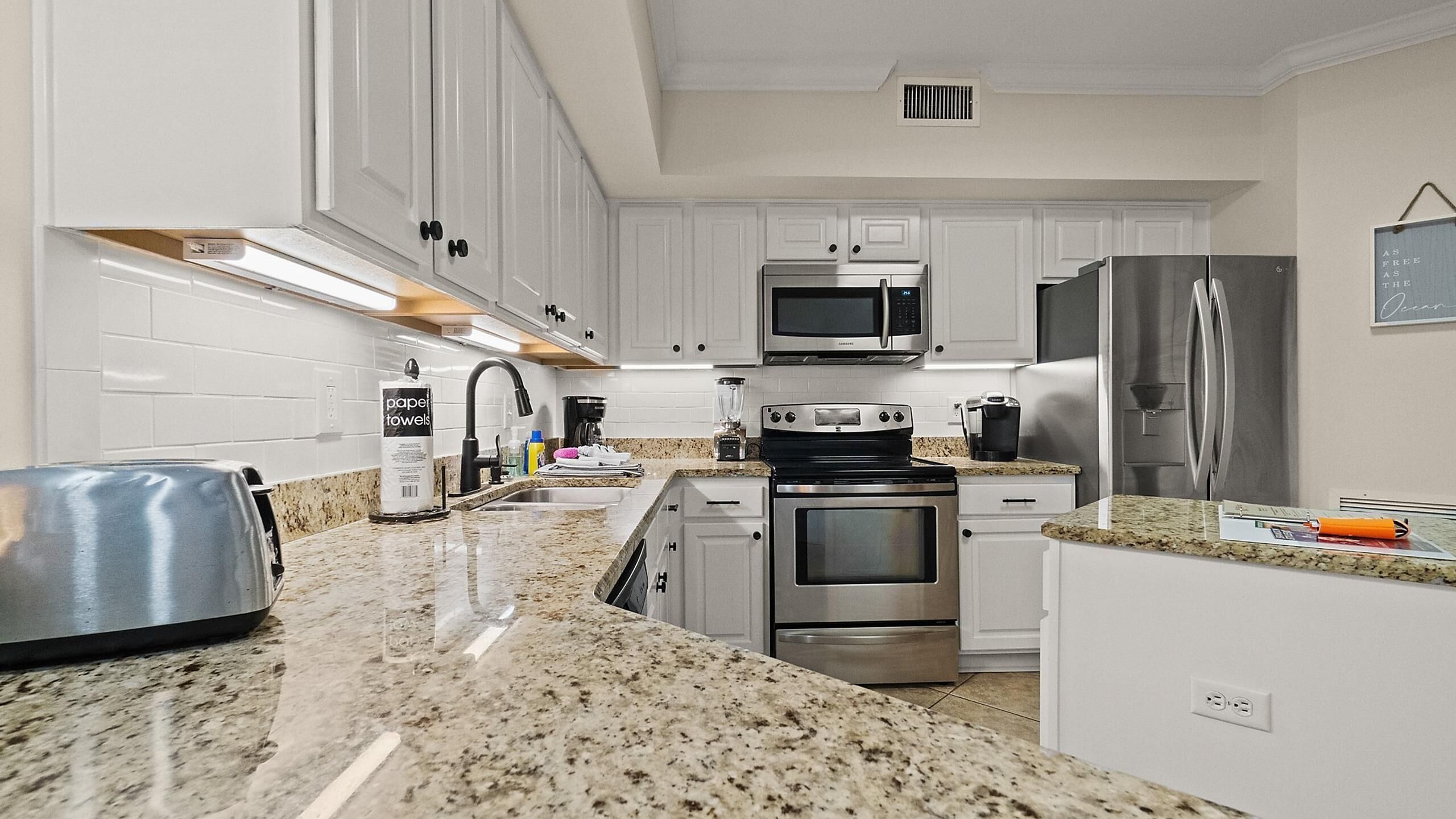 A modern kitchen with white cabinets, stainless steel appliances, granite countertops, and a built-in oven.