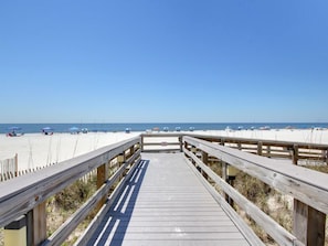 A wooden boardwalk leading to a sandy beach with umbrellas and beach chairs. - Pelican Pointe #1003 by Southern Vacation Rentals (Orange Beach)