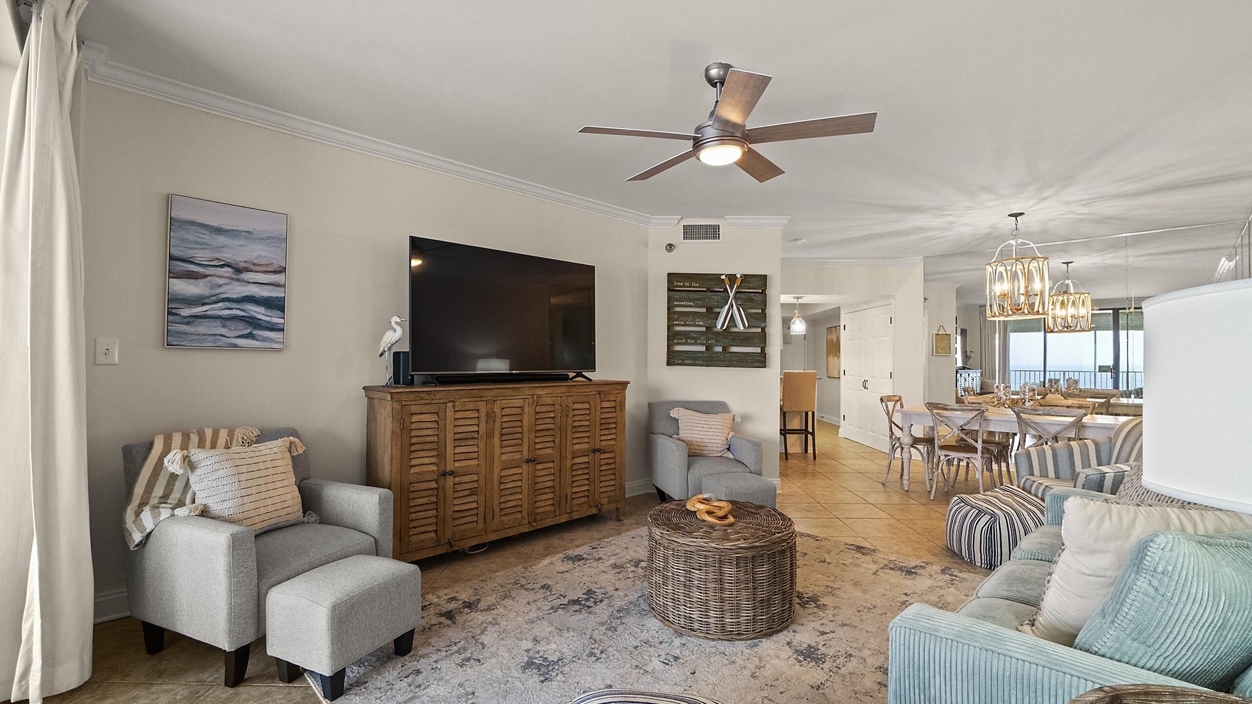 A spacious living room with a flat-screen TV, a wooden cabinet, and a ceiling fan.