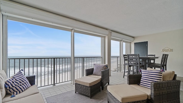 Un balcon avec des meubles en osier, une vue sur la plage et un panneau indiquant « PLAGE » sur le mur.