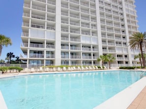 A multi-story hotel with balconies, a swimming pool, and palm trees. - Pelican Pointe #1003 by Southern Vacation Rentals (Orange Beach)