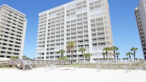 Un grand hôtel avec de nombreux balcons, situé près d’une plage bordée de palmiers.