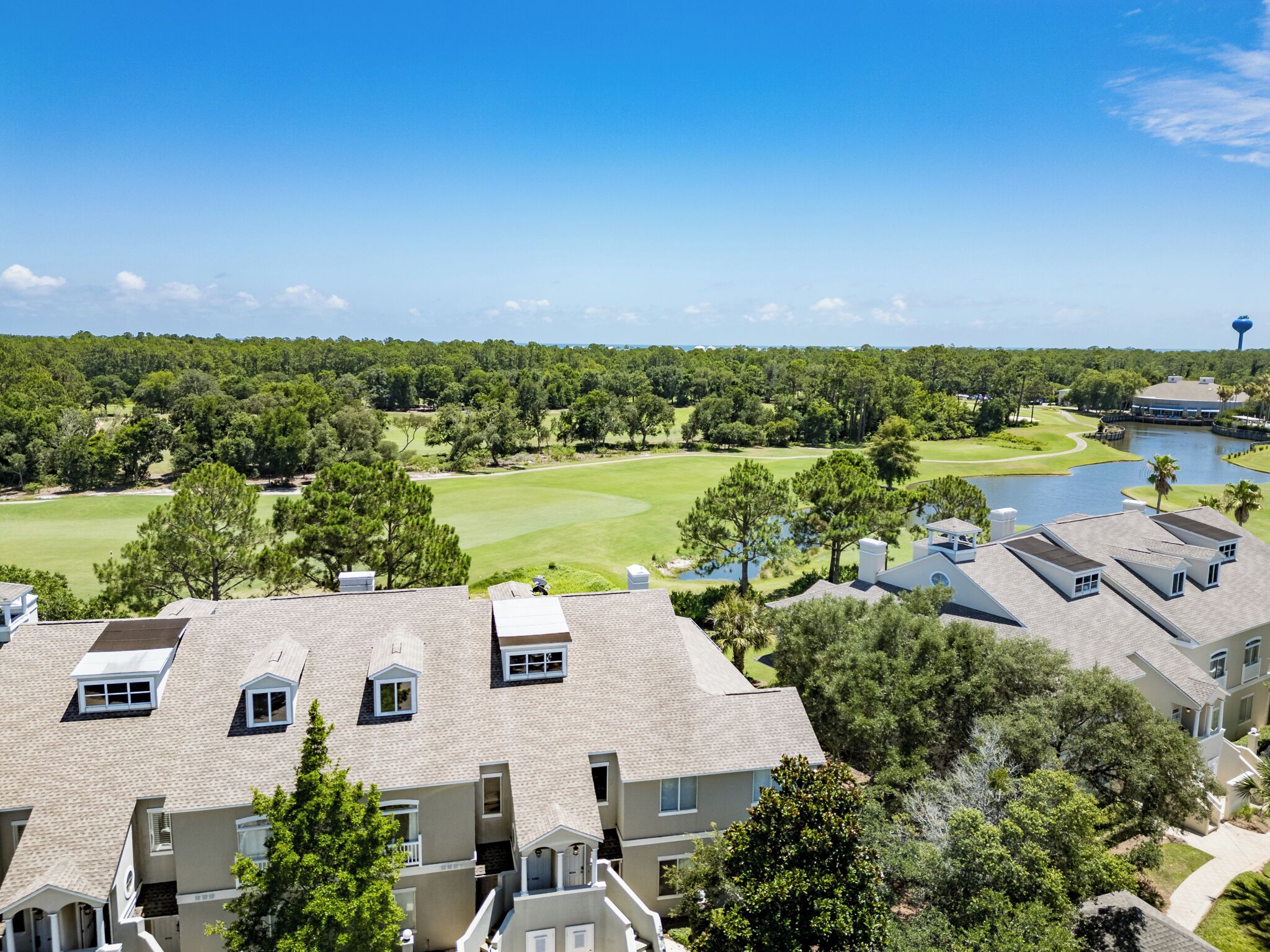 A residential area with multiple two-story houses, a golf course, and a body of water.