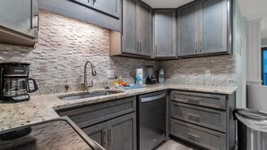 Una cocina moderna con armarios oscuros, encimera de granito y un rebozado de ladrillo.