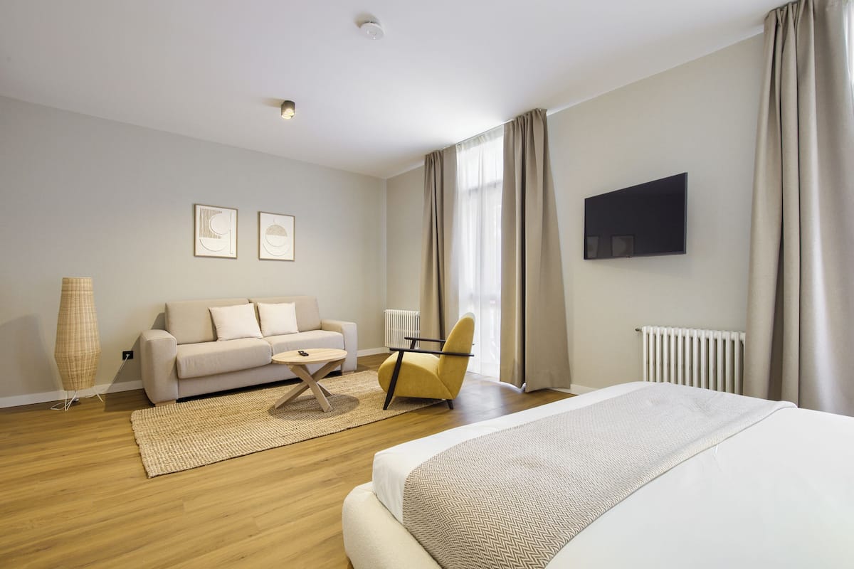 Une chambre d’hôtel moderne équipée d’un lit, d’un canapé, d’un fauteuil et d’une télévision.