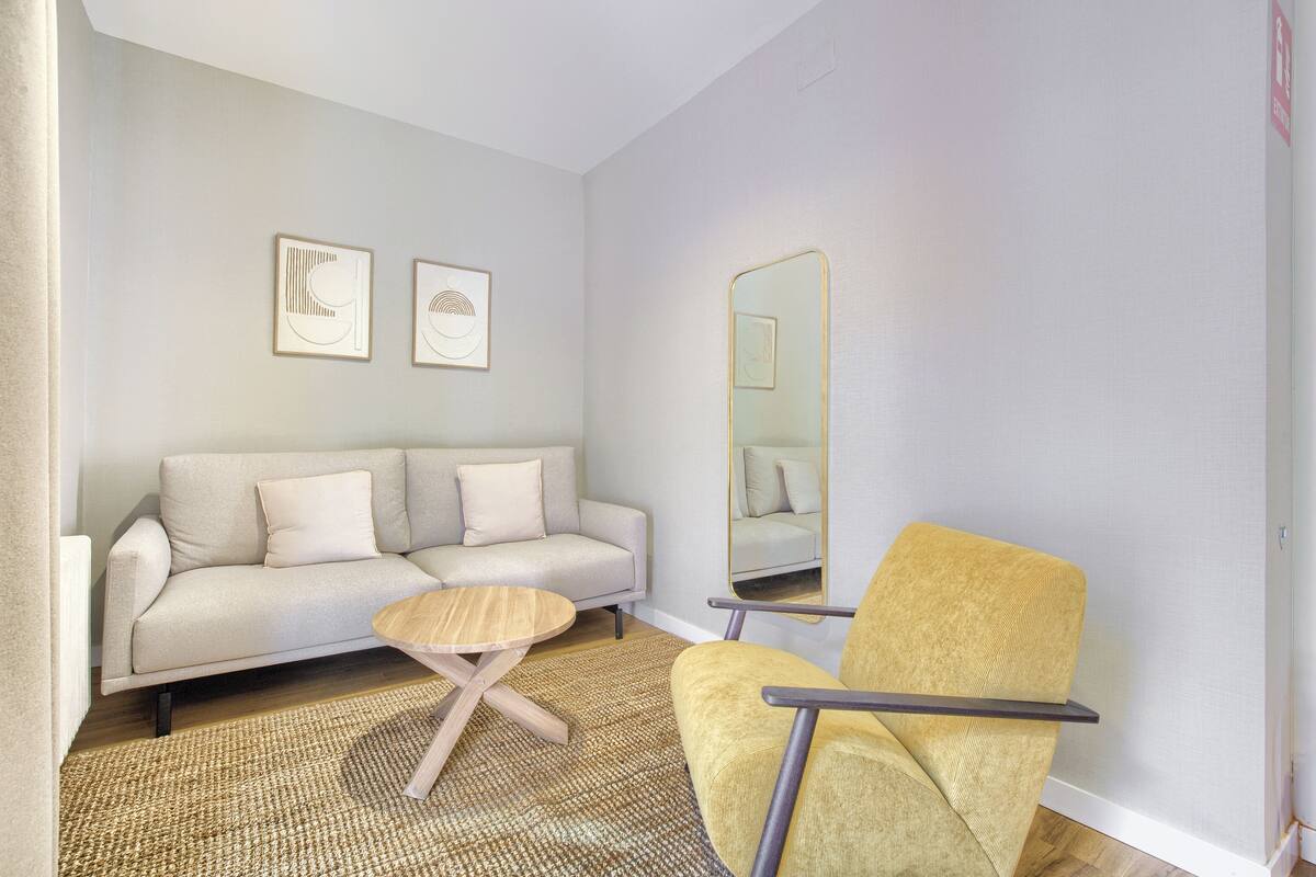 Un salon moderne avec un canapé, un fauteuil, une table basse ronde et un grand miroir.