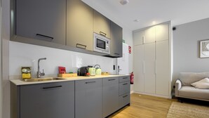 A modern kitchen with grey cabinets, a microwave, and a sink. There is a fire extinguisher on the wall and a sofa in the adjacent living area. - Dobo Madrid Justicia (Madrid)