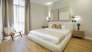 A bedroom with a large bed, a wooden chair, a nightstand, and a lamp. - Dobo Madrid Justicia (Madrid)