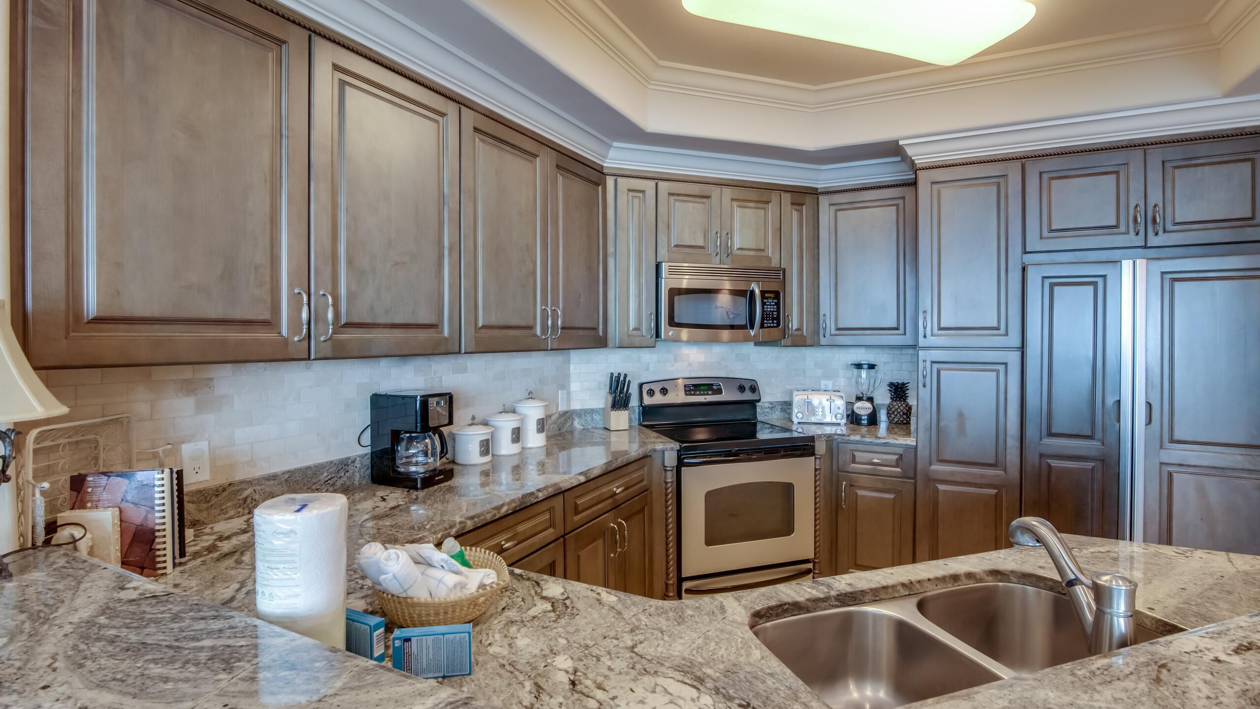 A kitchen with wooden cabinets, a stainless steel sink, a microwave, a stove, and various kitchen appliances.