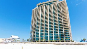A high-rise hotel with multiple balconies, located on a beach with a clear blue sky. - Phoenix West by Southern Vacation Rentals (Orange Beach)