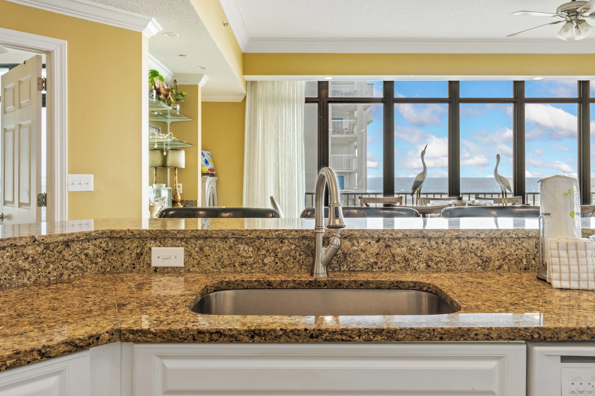 A kitchen with granite countertops, a stainless steel sink, and a view of the ocean through large windows.