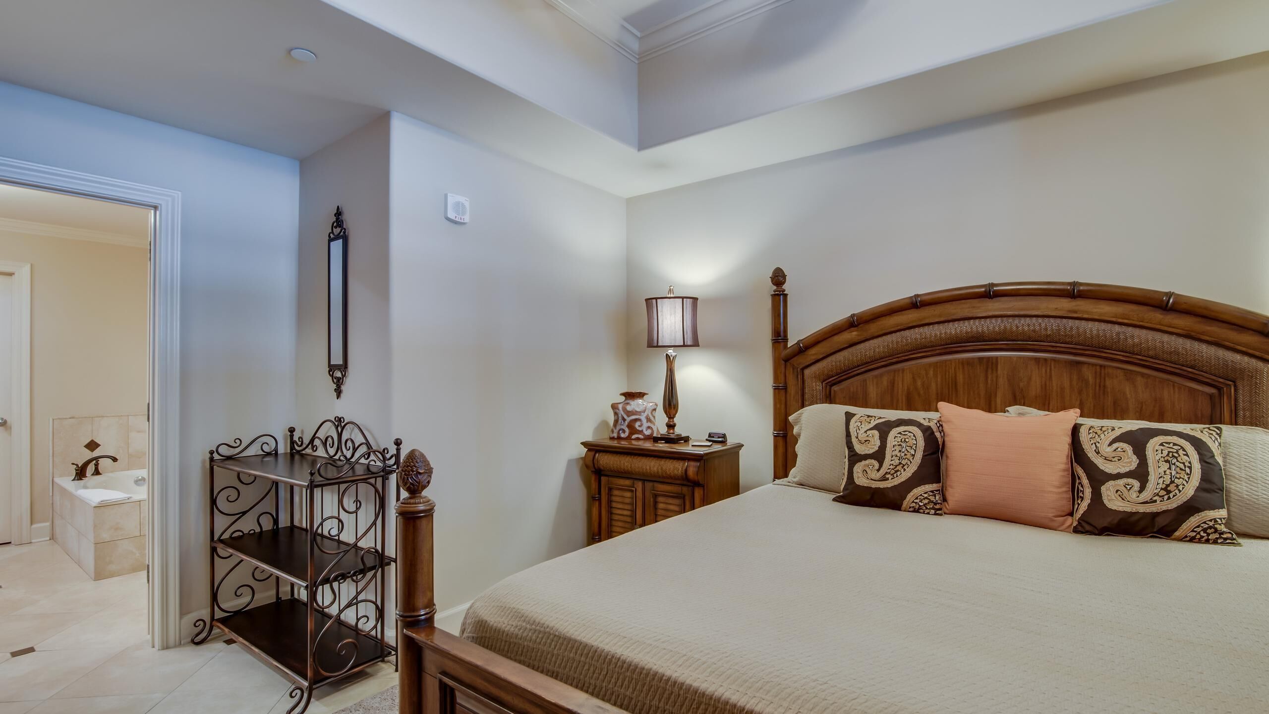 A bedroom with a wooden bed, a nightstand, a lamp, and a decorative mirror.