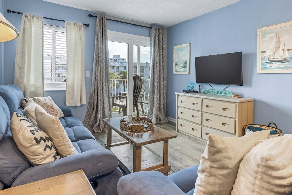 Ein Wohnzimmer mit einer Couch, einem Couchtisch, einem Fernseher und Blick auf den Balkon.