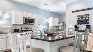 A modern kitchen with white cabinets, a central island, and bar stools. - Poseidon Palace by Southern Vacation Rentals (Gulf Shores)