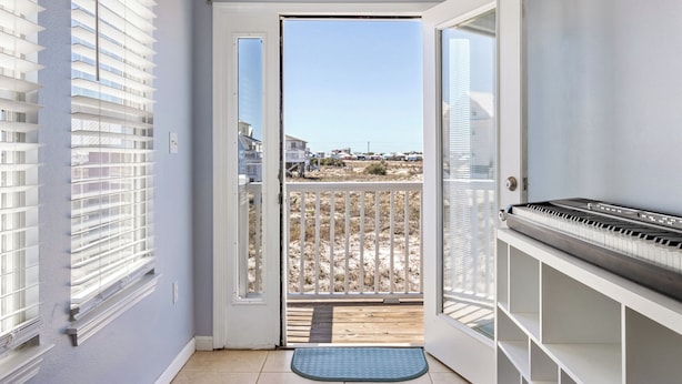 A balcony with a piano, a door leading outside, and a view of a sandy area. - Poseidon Palace by Southern Vacation Rentals (Gulf Shores)