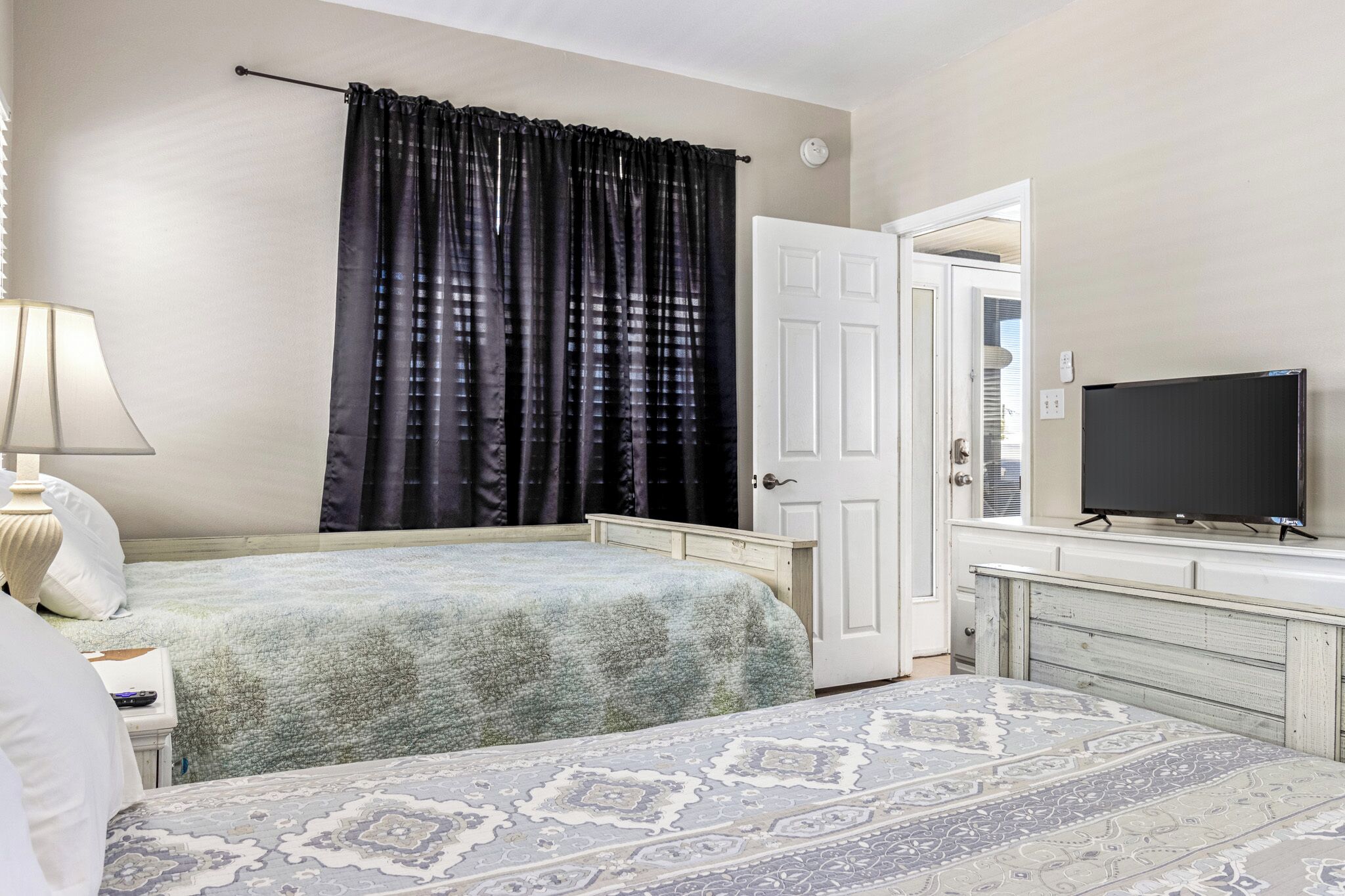 Een slaapkamer met twee bedden, een televisie, een lamp en een deur naar een andere kamer.