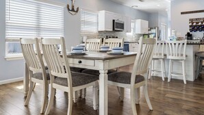 A modern kitchen with white cabinetry, a central island, and a dining area with white chairs. - Poseidon Palace by Southern Vacation Rentals (Gulf Shores)