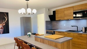 A modern kitchen with a central island, wooden cabinets, a Bosch microwave, and a stainless steel refrigerator. - Brand new apartment in Briançon, cable car access (Briançon)