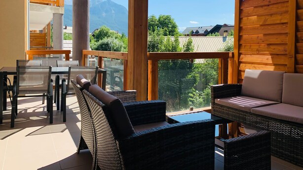 A sunlit balcony with wicker furniture, a glass table, and a view of mountains. - Brand new apartment in Briançon, cable car access (Briançon)