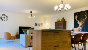 A modern living room with a wooden cabinet, a dining area with chairs, a TV, and artwork on the walls. - Brand new apartment in Briançon, cable car access (Briançon)