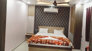 A hotel room with a bed, a ceiling fan, an air conditioning unit, and a patterned wall. - Hotel Regal Heights (Deoghar)