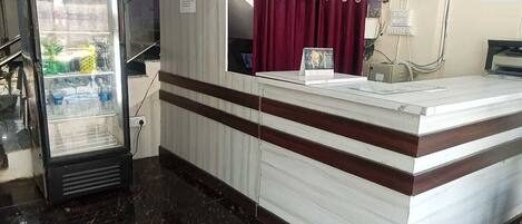 A reception area with a counter, a refrigerator, a clock, and a window with curtains.