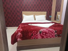 Una cama bien hecha con sábanas blancas y una colcha estampada de flores rojas, en una habitación con pared de estampado rojo y cabecero de madera.