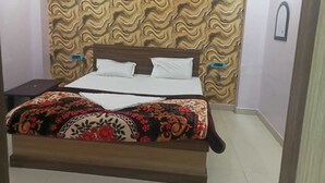 A neatly made bed with a floral bedspread, a wooden headboard, and a patterned wallpaper. - Hotel Regal Heights (Deoghar)