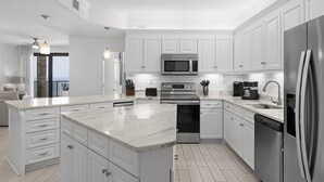 Una cucina moderna con mobili bianchi, elettrodomestici in acciaio inossidabile e una grande isola con piano di lavoro in marmo.