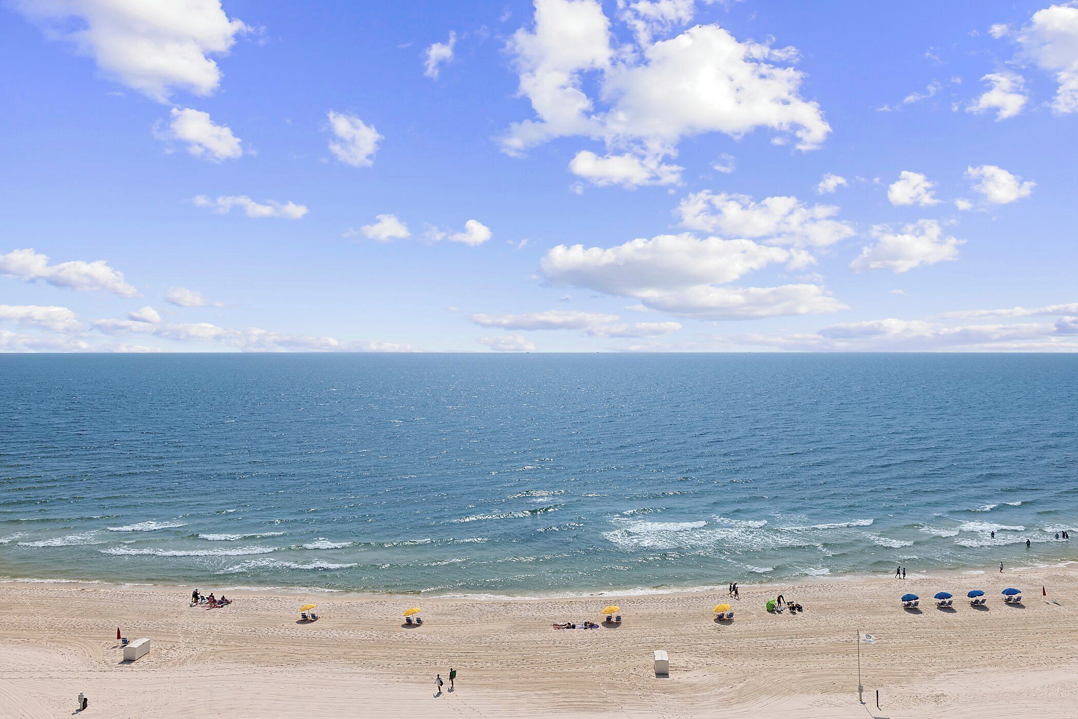 A beach with people sunbathing and swimming, and a clear blue sky.