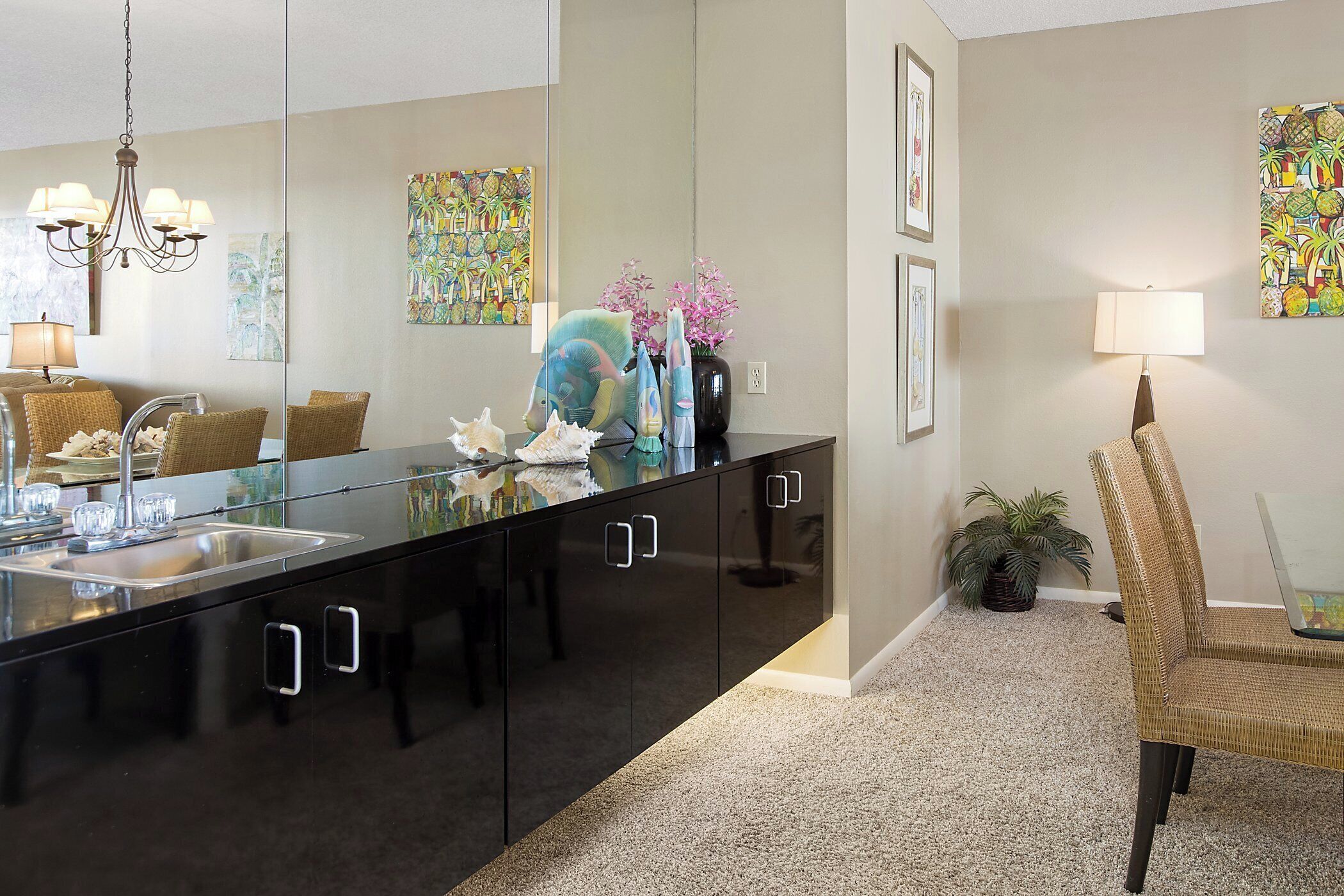 A modern kitchen with a black countertop, stainless steel sink, and a large mirror above the counter.