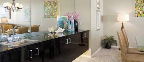 A modern kitchen with a black countertop, stainless steel sink, and a large mirror above the counter.