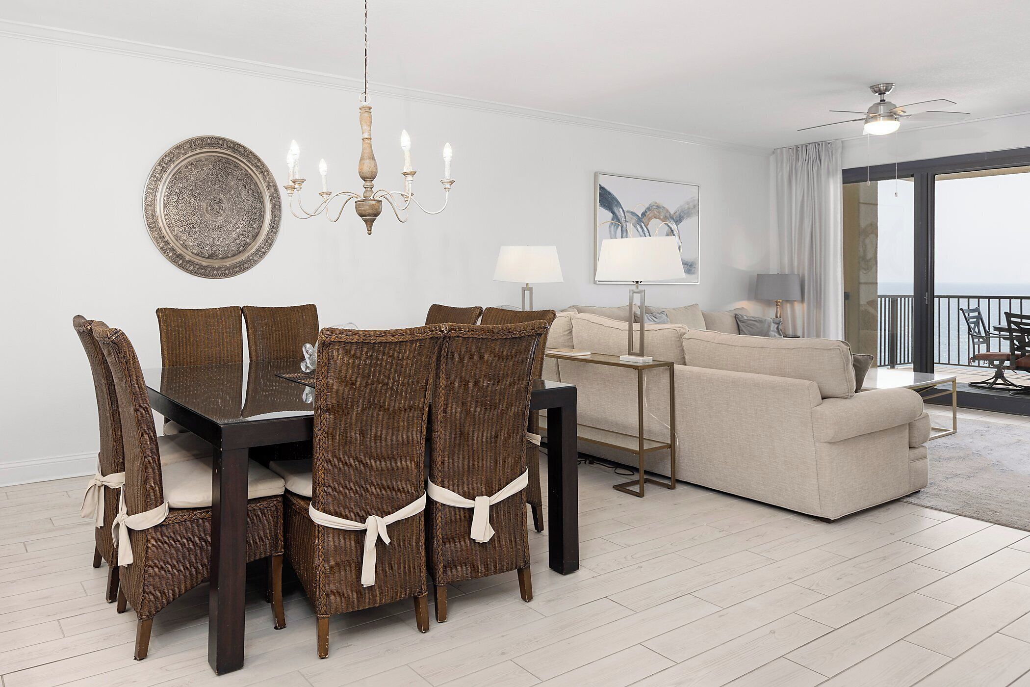 A dining area with a table and chairs, a sofa, a lamp, and a view of the balcony.