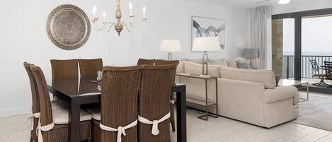 A dining area with a table and chairs, a sofa, a lamp, and a view of the balcony.