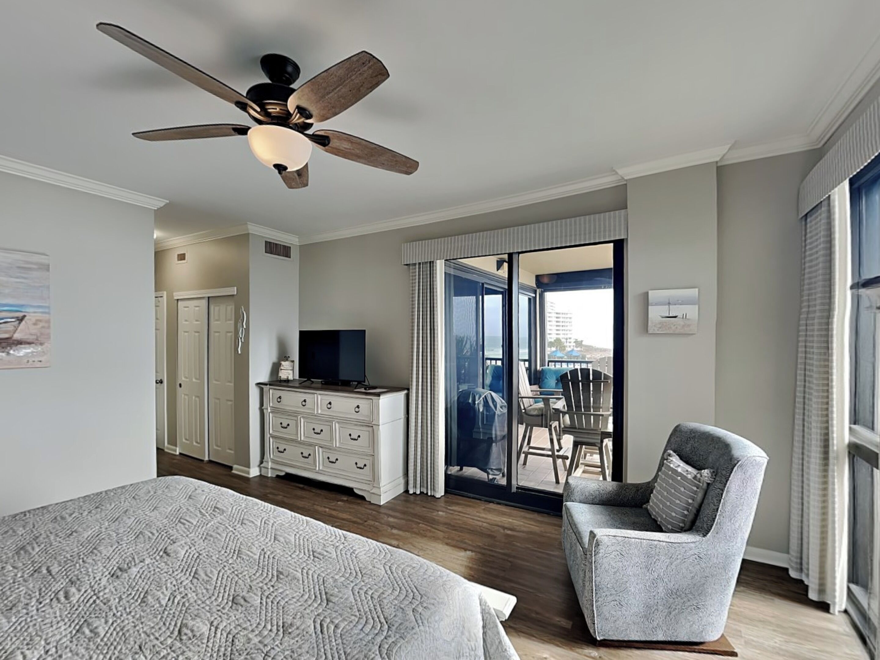 Une chambre à coucher comprenant un lit, une chaise, une commode, un téléviseur et un balcon avec vue.