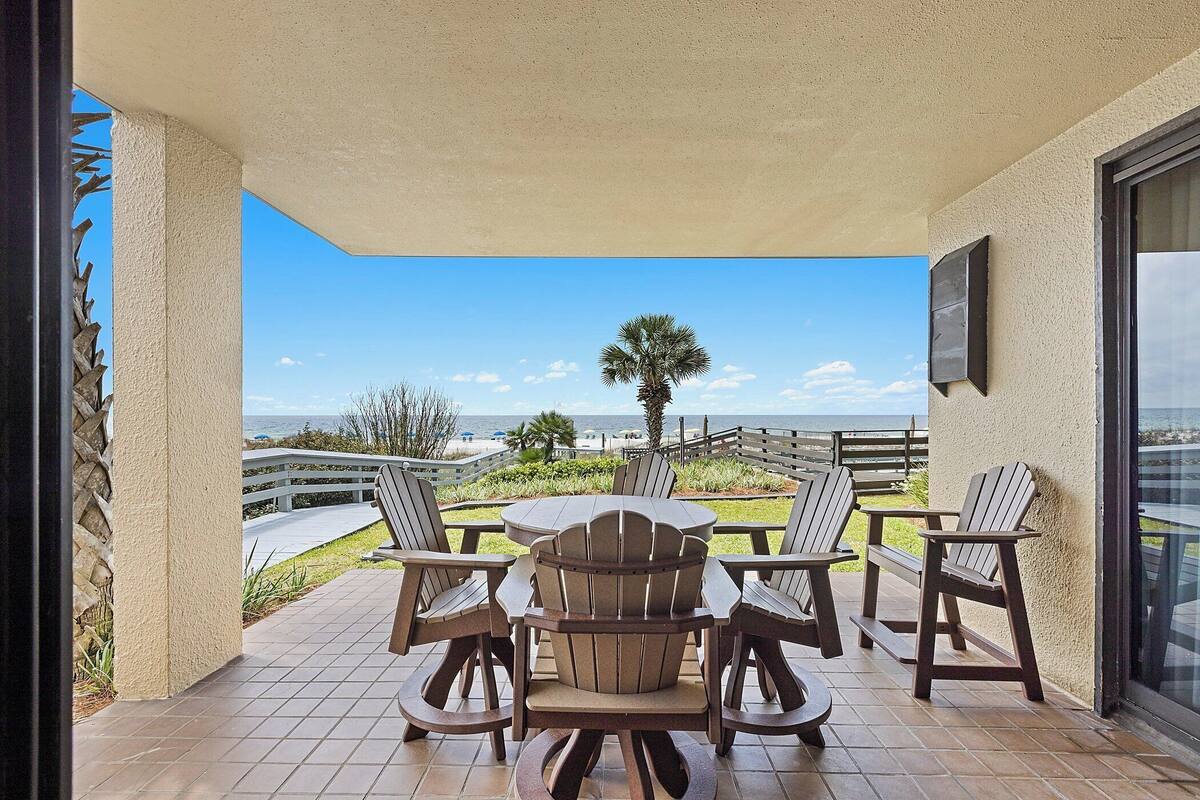 Een terras met een tafel en stoelen, uitzicht op de oceaan en een palmboom.