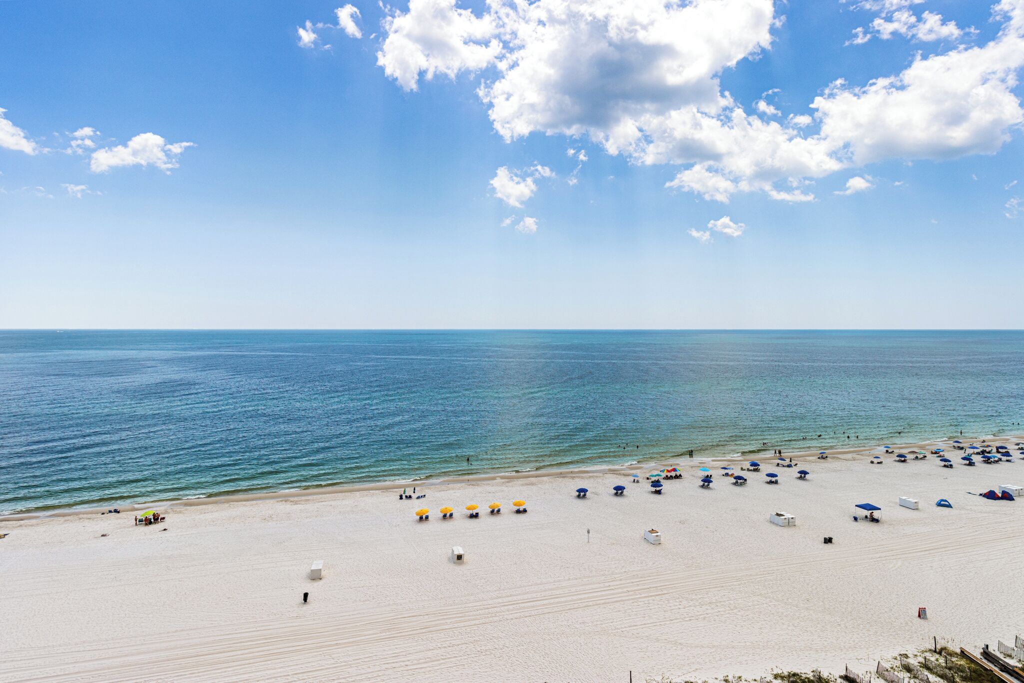 A beach with a clear sky and calm sea. There are several umbrellas and beach chairs on the sand.