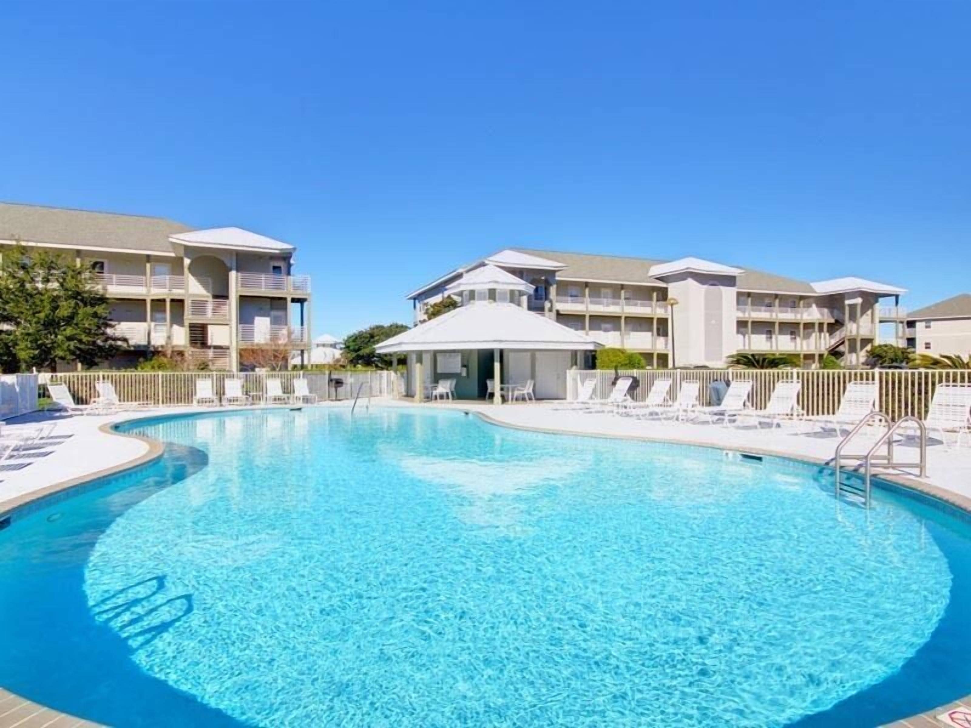 Una piscina circondata da poltroncine bianche e un’area relax coperta, con edifici a più piani sullo sfondo.