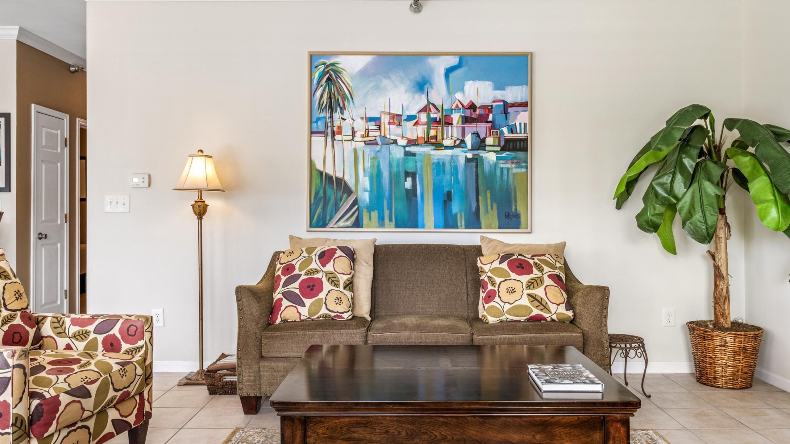 A living room with a sofa, armchair, coffee table, floor lamp, and a large potted plant.