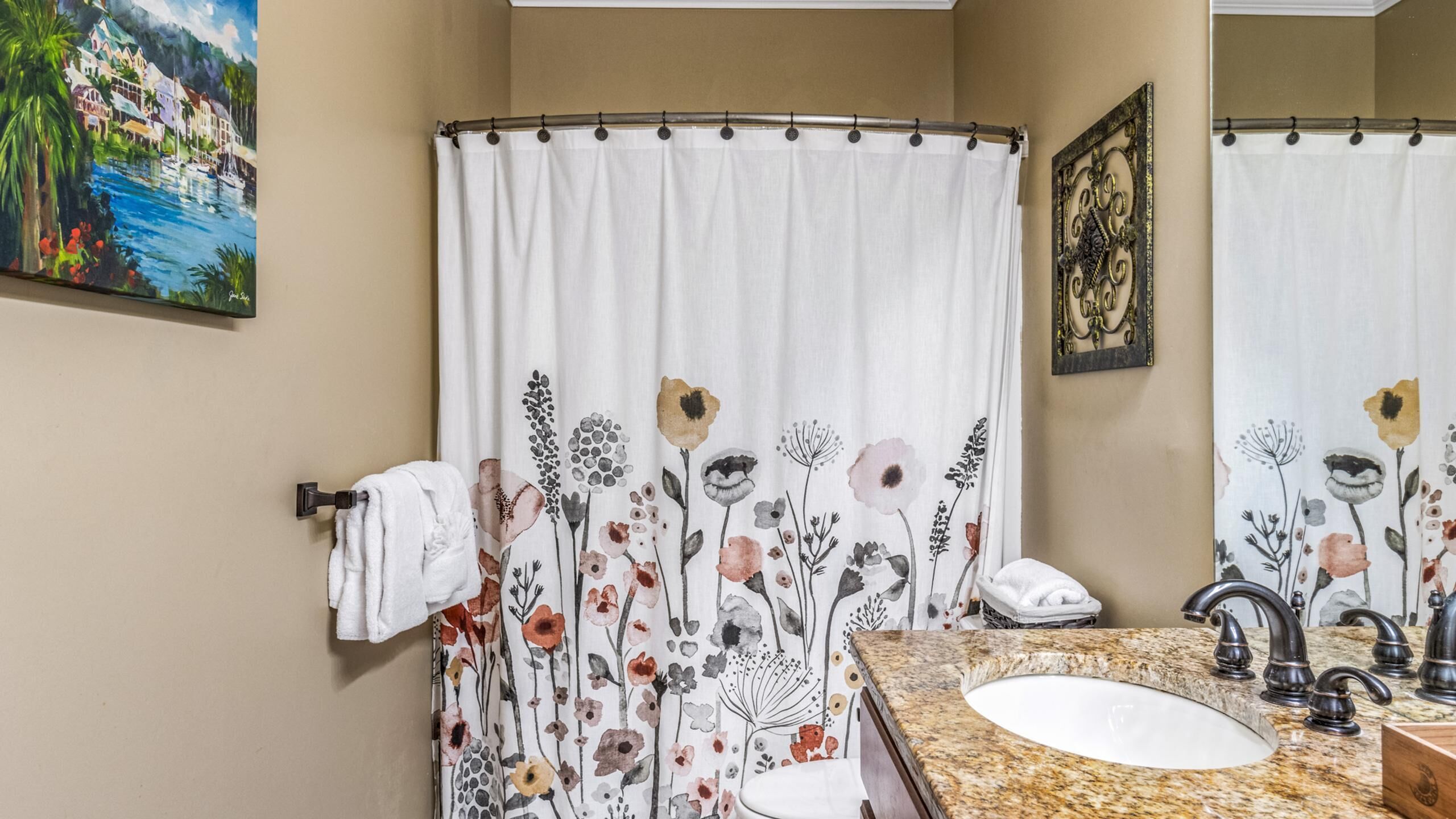 Casa de banho com cortina de chuveiro estampada com flores, pia com bancada de granito e espelho com moldura decorativa.