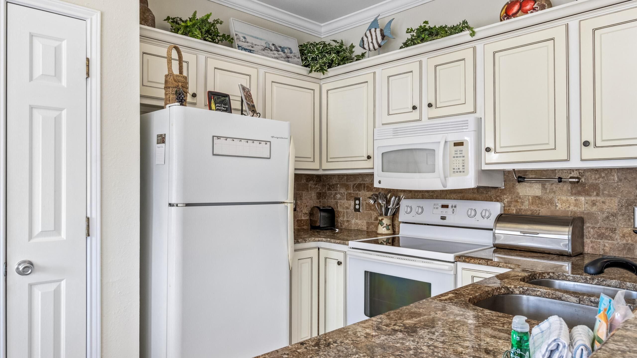A kitchen with white cabinets, a refrigerator, a microwave, a toaster, an oven, and a sink.