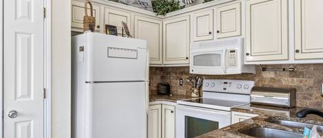 A kitchen with white cabinets, a refrigerator, a microwave, a toaster, an oven, and a sink.