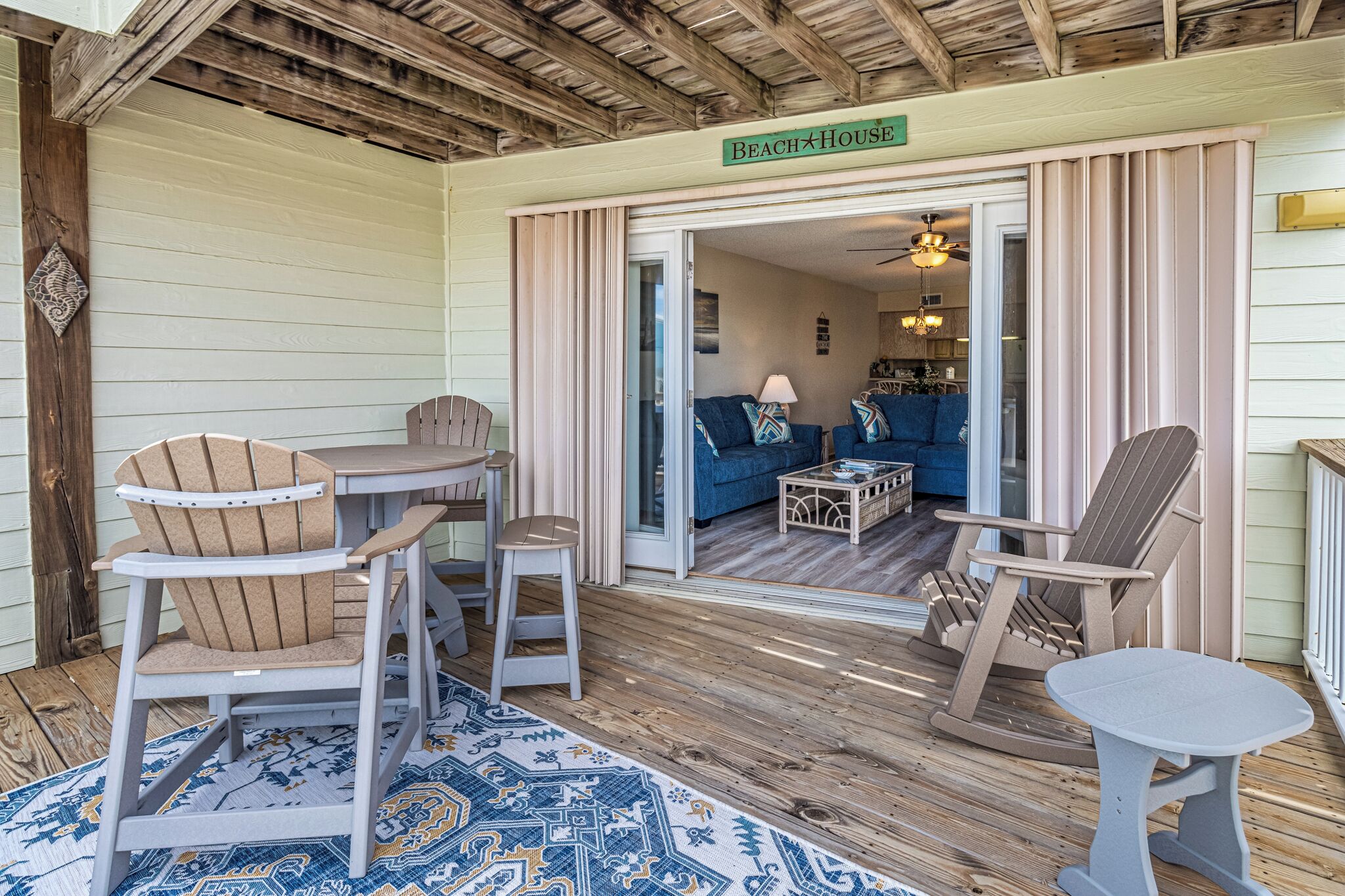 A wooden deck with Adirondack chairs, a small table, and a rug.