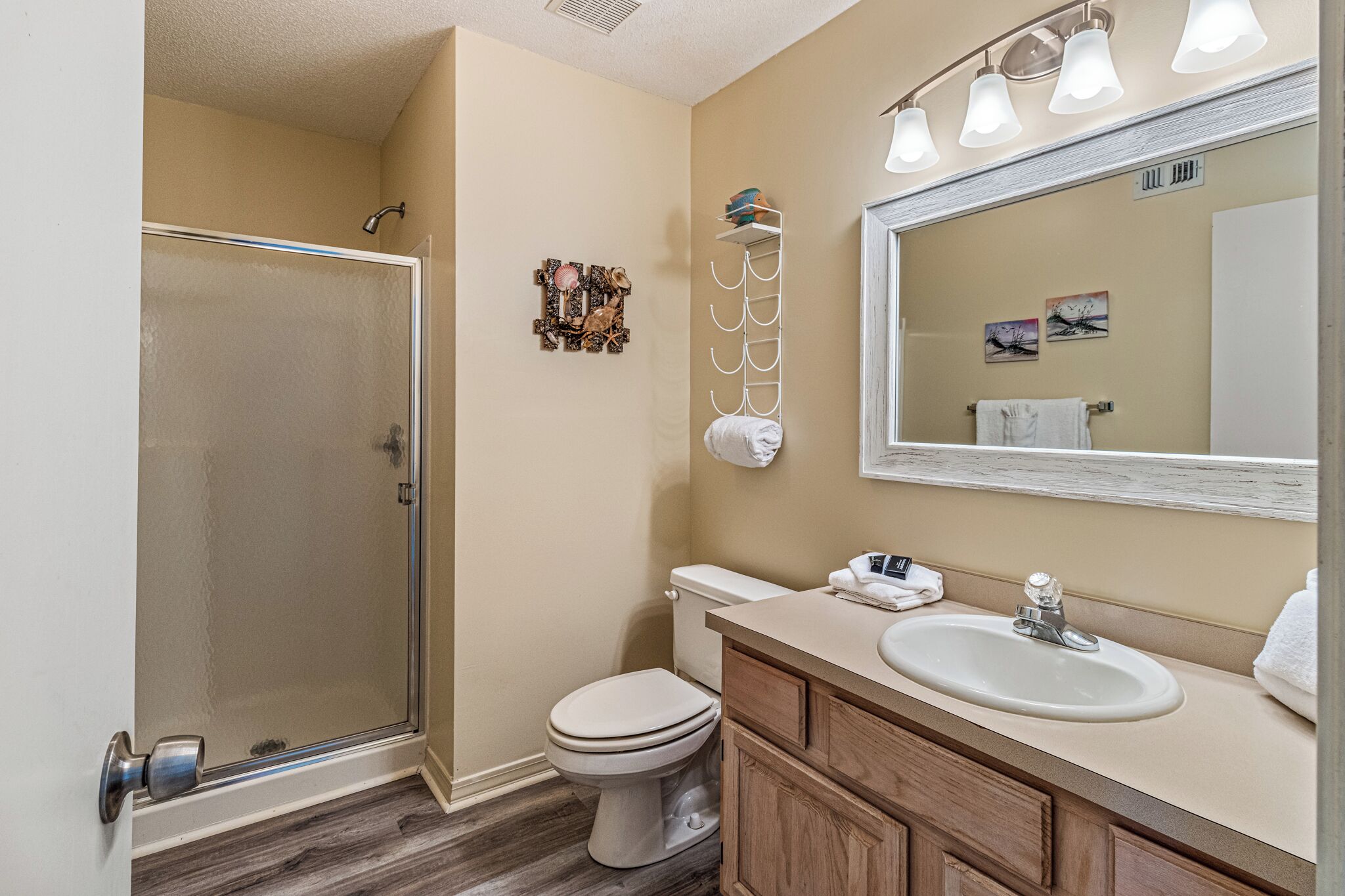 A bathroom with a glass shower enclosure, a toilet, a sink with a vanity, and a mirror with lights.