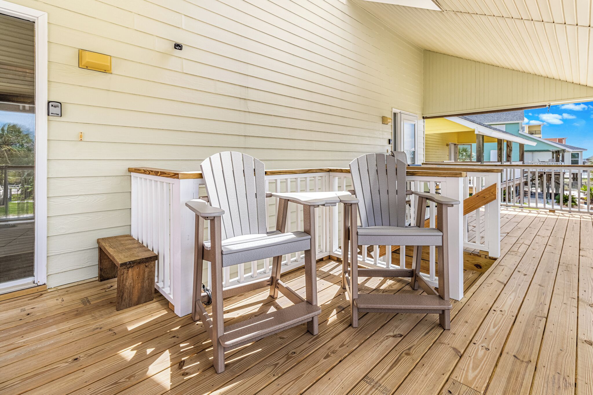 A covered wooden deck with Adirondack chairs and a small wooden stool.