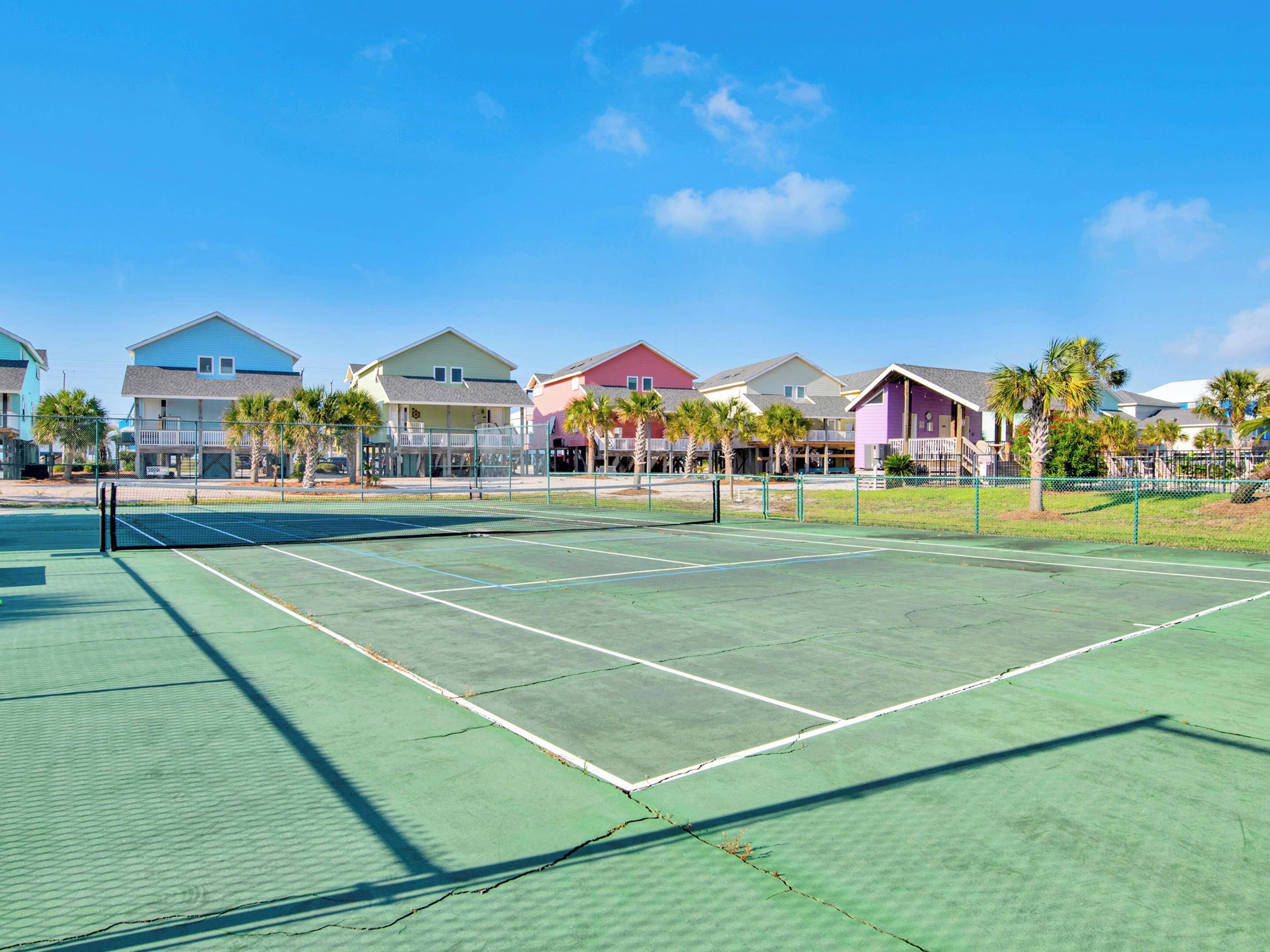 Una cancha de tenis con red, rodeada de casas y palmeras.