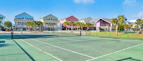 Una cancha de tenis con red, rodeada de casas y palmeras.